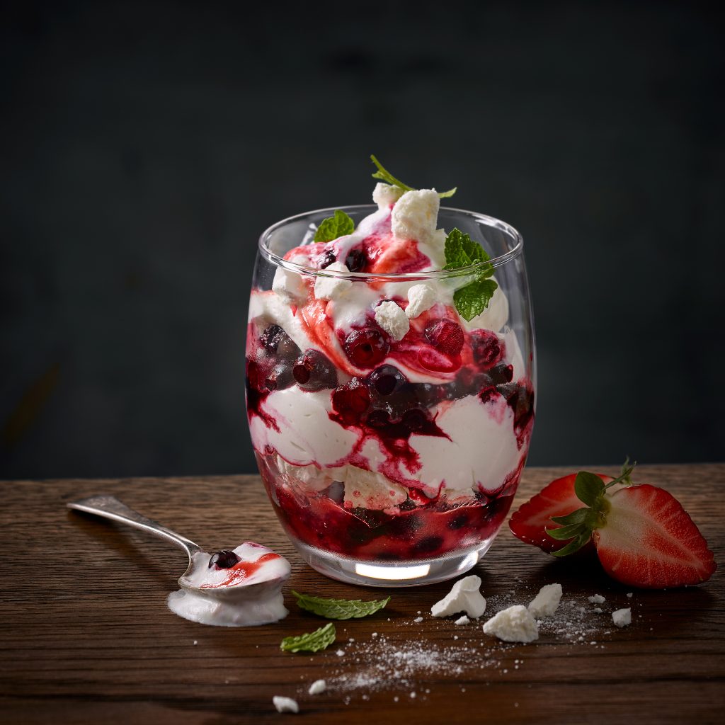 Desserts eton mess im glas mit löffel erdbeeren und puderzucker am holztisch foodfotografie