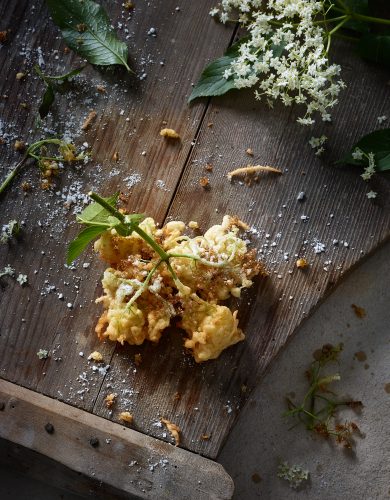 dark food photography of deep-fried Elderbossom on weathered Wood blossoms leafs