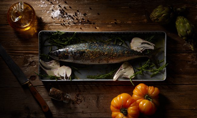 Image Produktfotos makrele fisch liegt in metalschale aussenrum zutaten tomaten artischocke knoblach salz pfeffer algen messer dunkler holzuntergrund