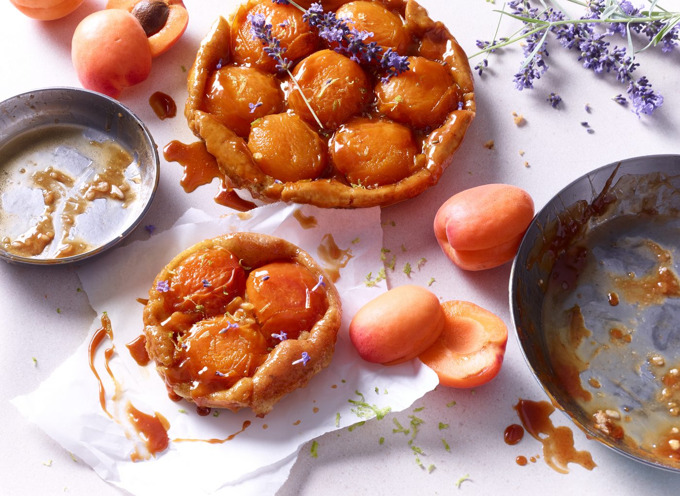 kuchen tarte tatin aprikose liegt gestuerzt auf zerknicktem Kuechenpapier kuchenformen liegen daneben ganze und halbierte aprikosen als Deko daneben foodfotografie foodphotography munich muenchen vogelperspektive heller lebendiger holzuntergrund