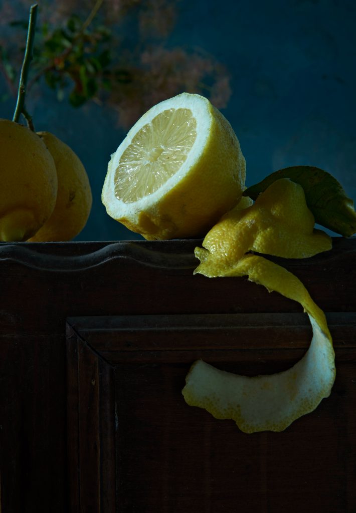 durch geschnittene Zitrone liegt auf altem Holztisch. Dicke Schale und Blatt der Zitrone liegen daneben. Das Bild wirkt wie ein altes Ölgemälde. Desserts in Vorbereitung