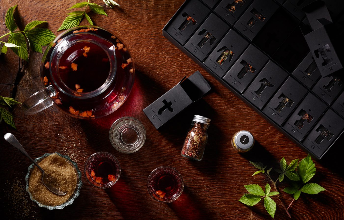 Image Produktfotos Tee Variationen Teekanne und Teeglas mit Himbeerblättern und Packund liegen auf warmem Holz Imageaufnahme