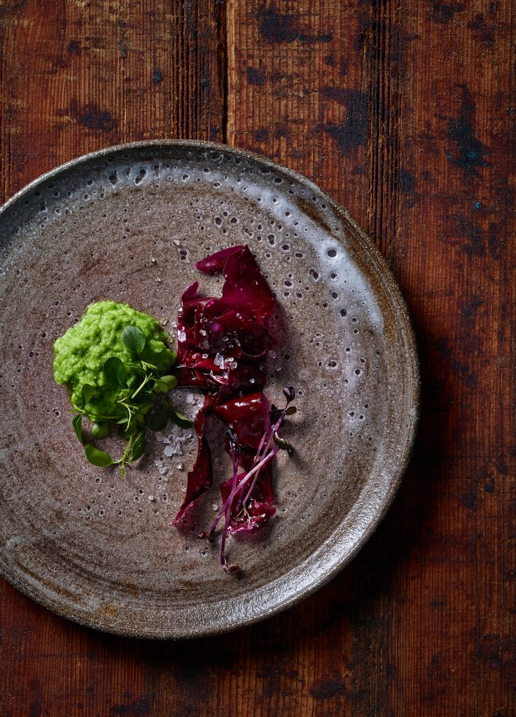 Japanisches Foodstyling algensalat mit erbsenpaste und salz auf getoepfertem teller alter speckiger lebendiger holzuntergrund tisch pure inszinierung