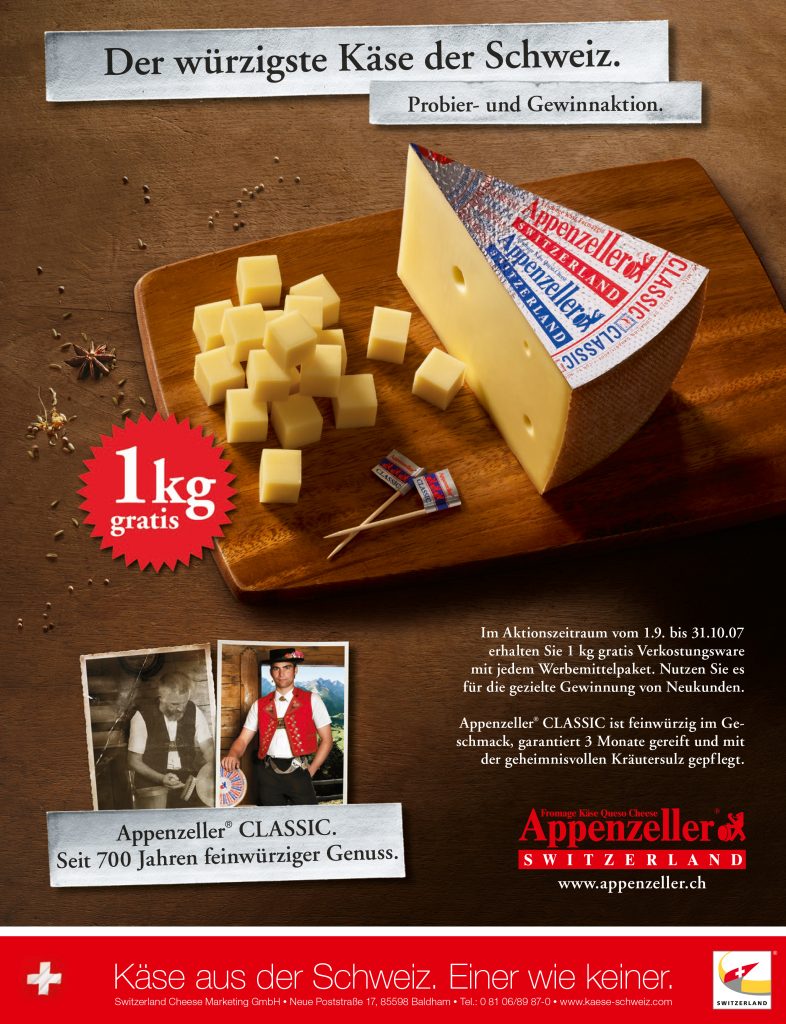 Scheibe aus Käselaib geschnitten steht auf altem Hoztisch mit Trauben daneben