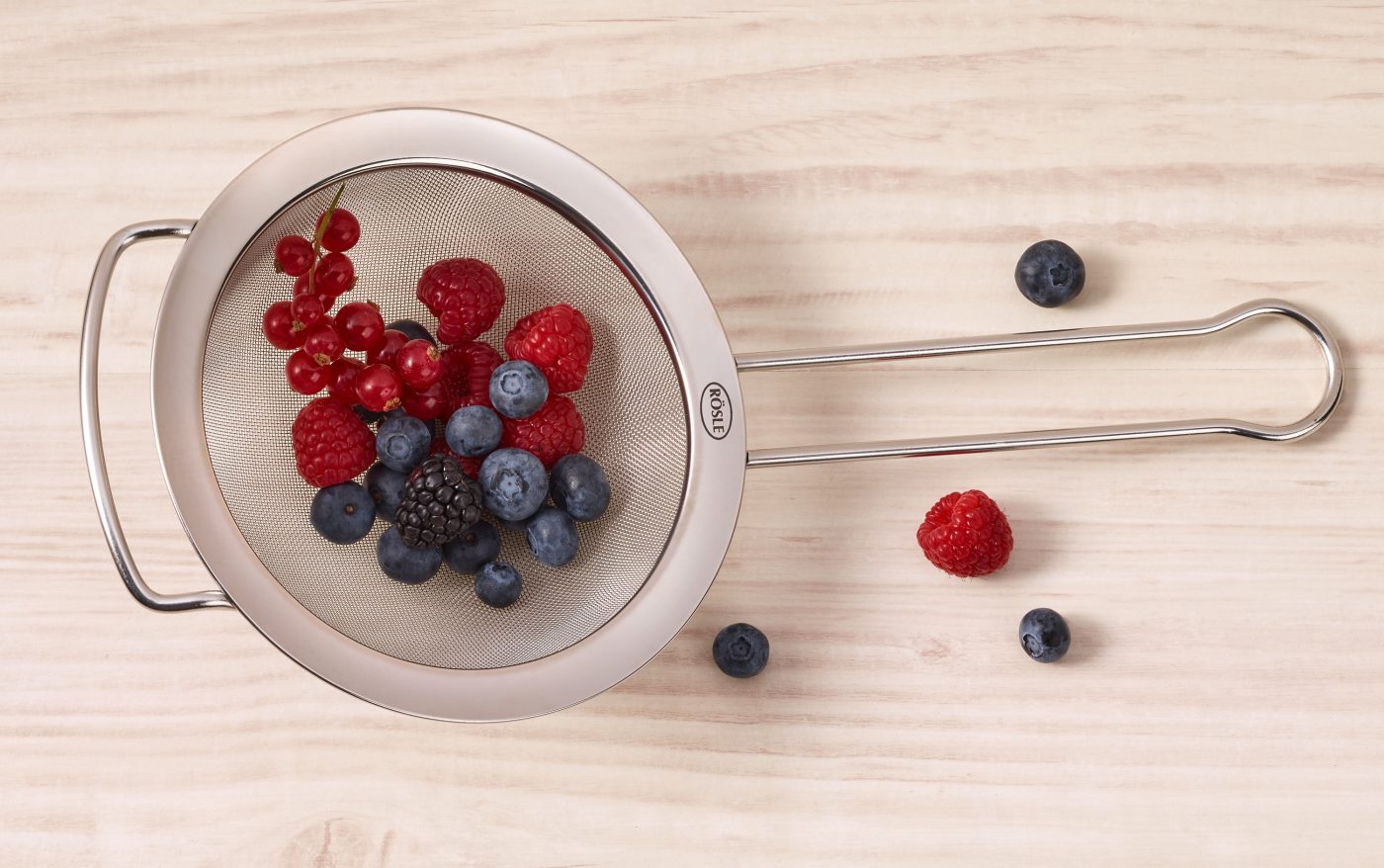 Food-Verpackungen mit Küchensieb. In dem liegen frisch gewaschene Waldbeeren. Es ist mit Tautropfen benetzt