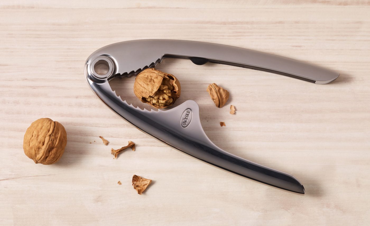 Food-Verpackungen eines Nussknackers der eine Walnuss geöffnet hat. Es liegen Teiler der Schale auf einem Holzuntergrund