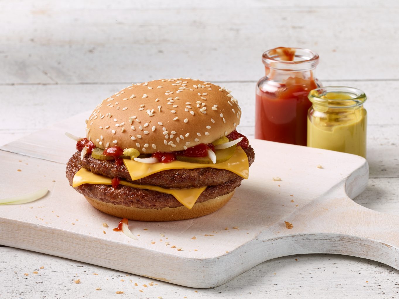 Local Store Marketing Foodshot of a Double Royal Cheese Burger with two Sauces Ketchup and Mustard in a glass on a white wooden board
