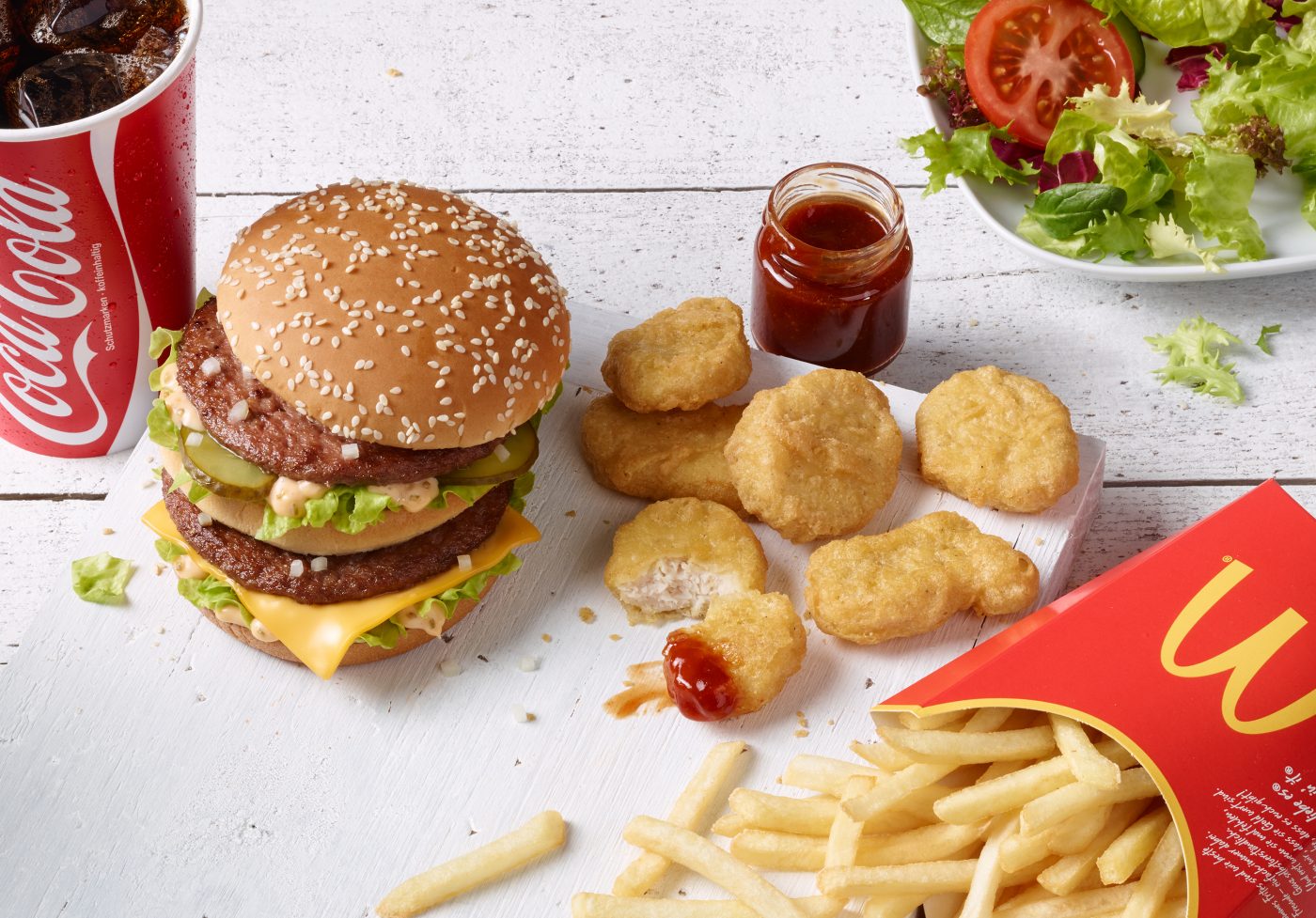 Local Store Marketing Bigmac French Fries Chicken mc nuggets Barbecue Sauce Salad lie on a wooden Underground which is painted white