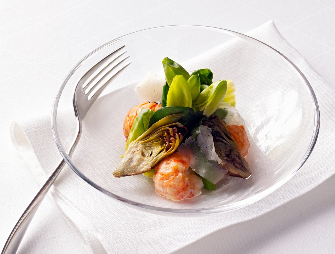 Verpackungsaufnahmen mit Artischocken Meeresfrüchten Salat in einer Glasschüssel. Eine Gabel liegt daneben, die Schüssel steht auf einer weissen Serviette