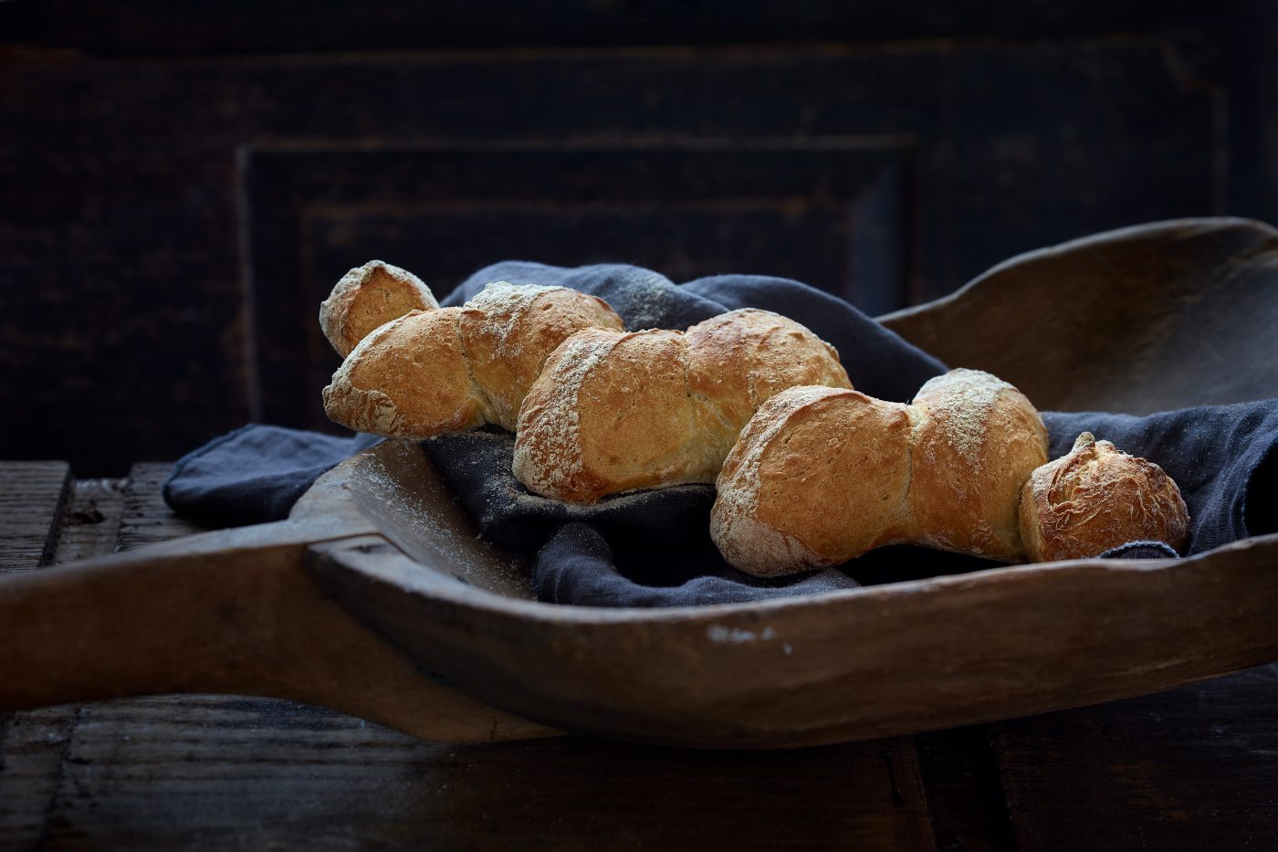 warmes Brot liegt mit dunklem Tuch auf alter Getreideschaufel aus Holz. Die Stimmung ist dunkel.