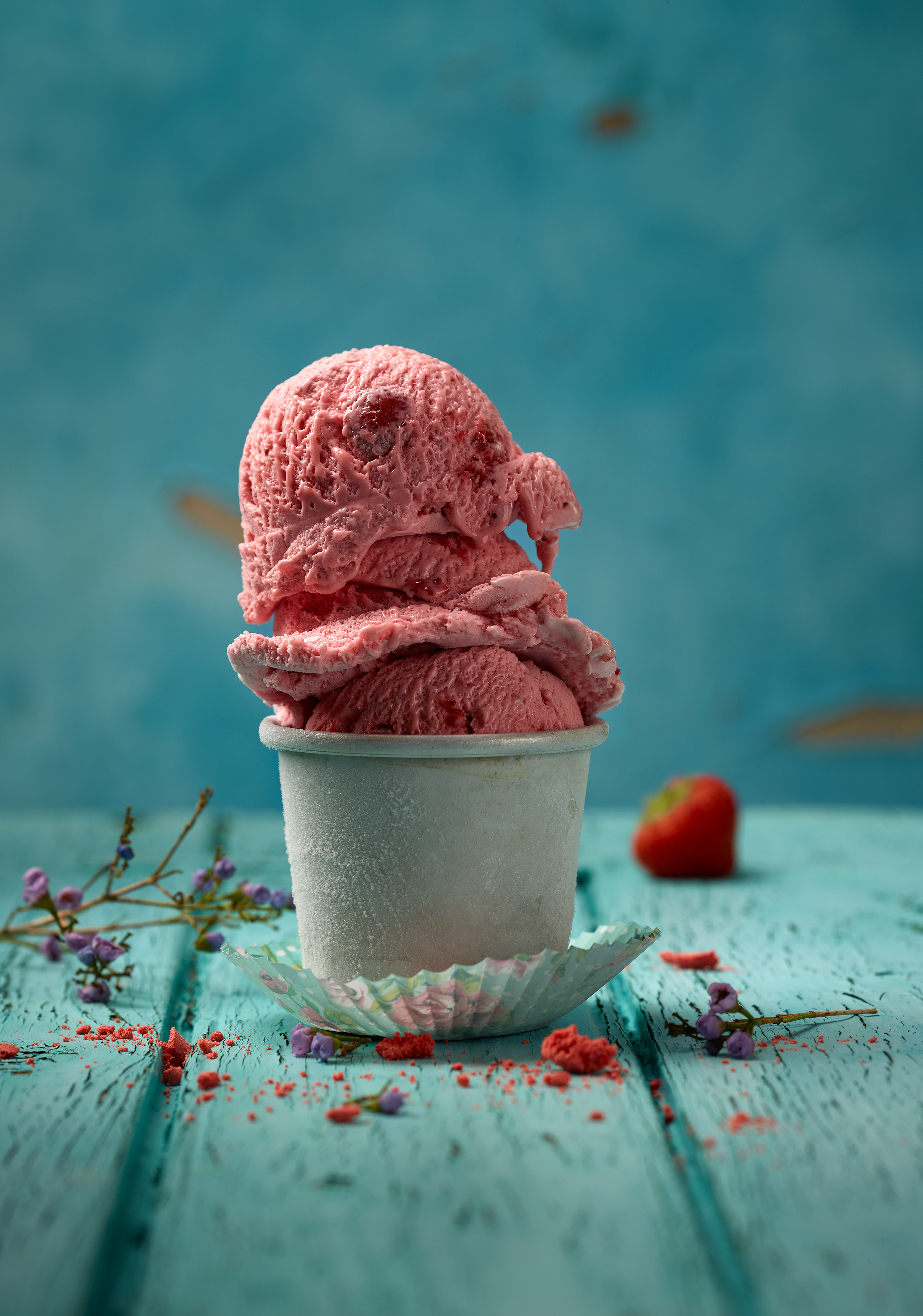 Three scoops of strawberry ice cream are in an iced shell. This stands on a colored baking paper. turquoise painted wooden board as background, blue background