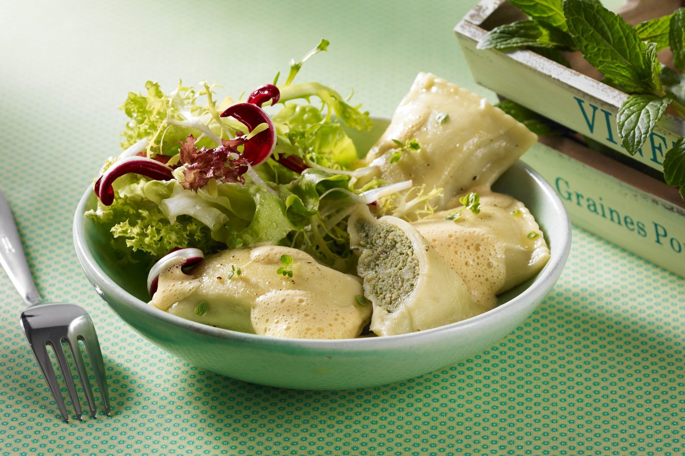 Packaging für Bio Maultaschen. Maultaschen mit Salat in einer grünen Schüßel. Grüne Tischdecke mit Deko