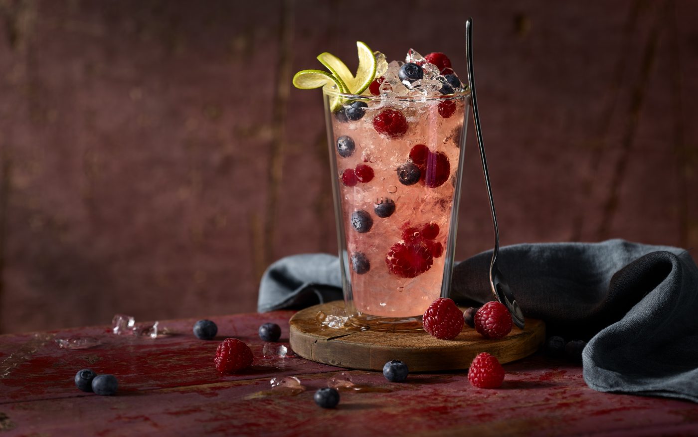 Tee Wild Berry ist im Glas mit Eiswürfeln Himbeeren Blaubeeren. Es ist ein leckes Cocktail Rezept. Hintergrund und Untergrund sind stylisch wie bei Instagram es liegt noch eine Serviette im Hintergrund