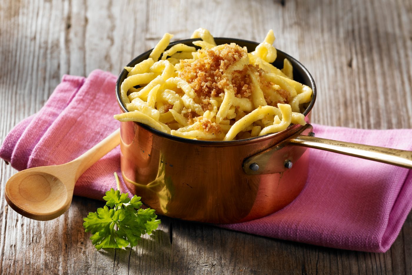 Packaging Foto für die Firma Bürger GmbH. Die Eierspätzle sind in einer Kupferkasserole, darunter ist eine rote Serviette. Auf dem alten Holztisch liegt eine grüne Petersilie.