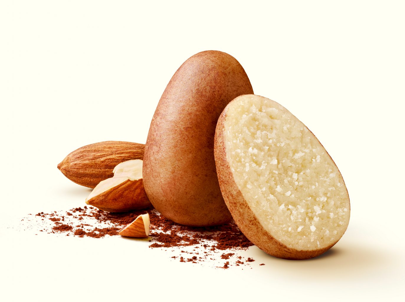 One whole and one half confectionery marzipan egg with two almonds on a beige background