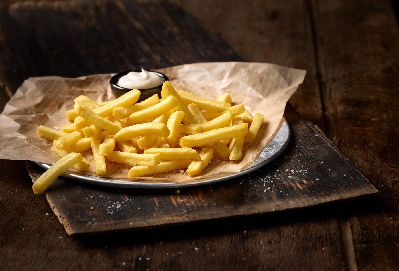 freshly prepared french fries on a paper with mayonaise.