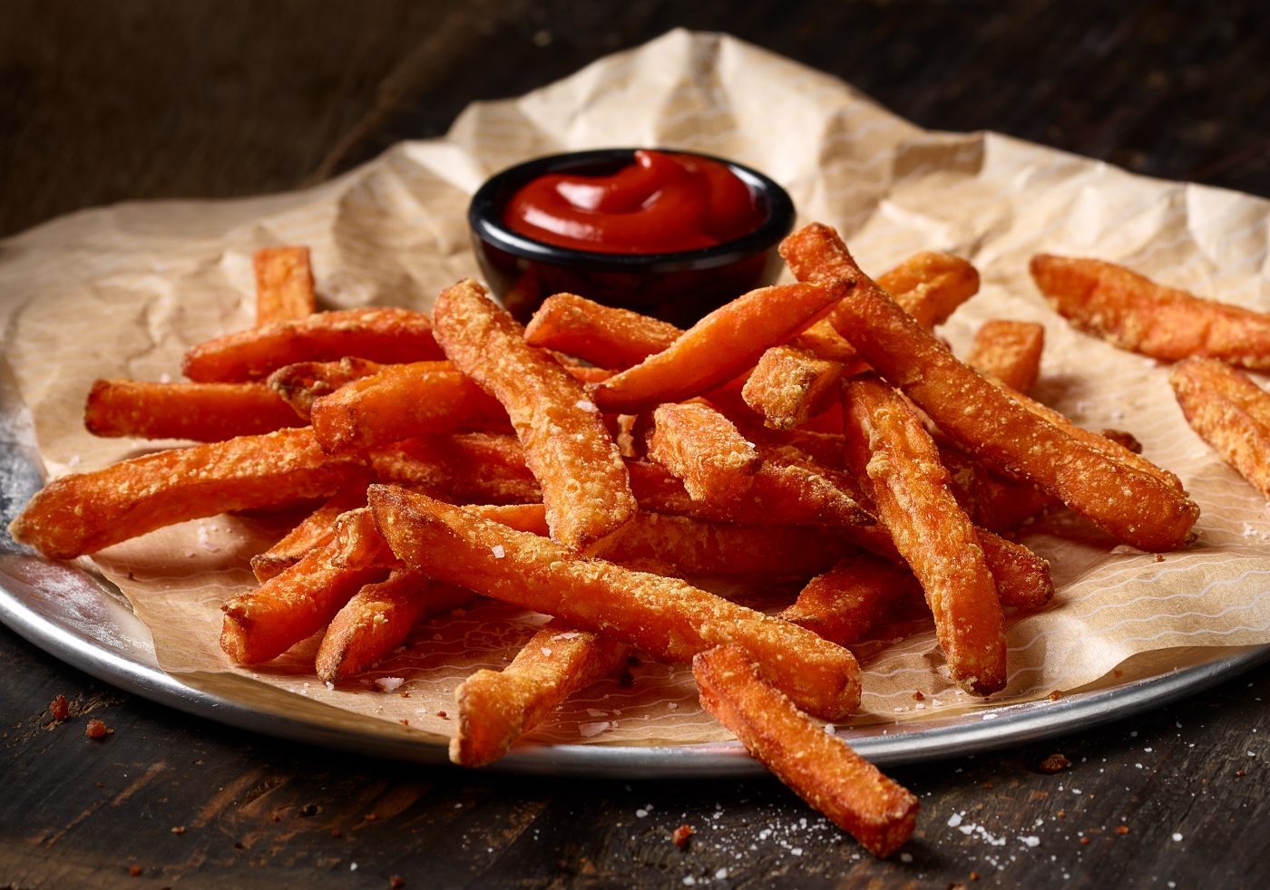 freshly prepared sweet potatoes french fries lieing on a paper with ketchup