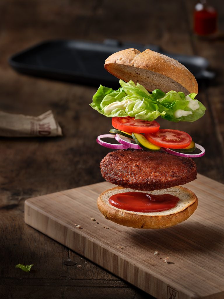 freshly prepared vegan good Burger is seen in an explosion. all the ingredients are flying through the air