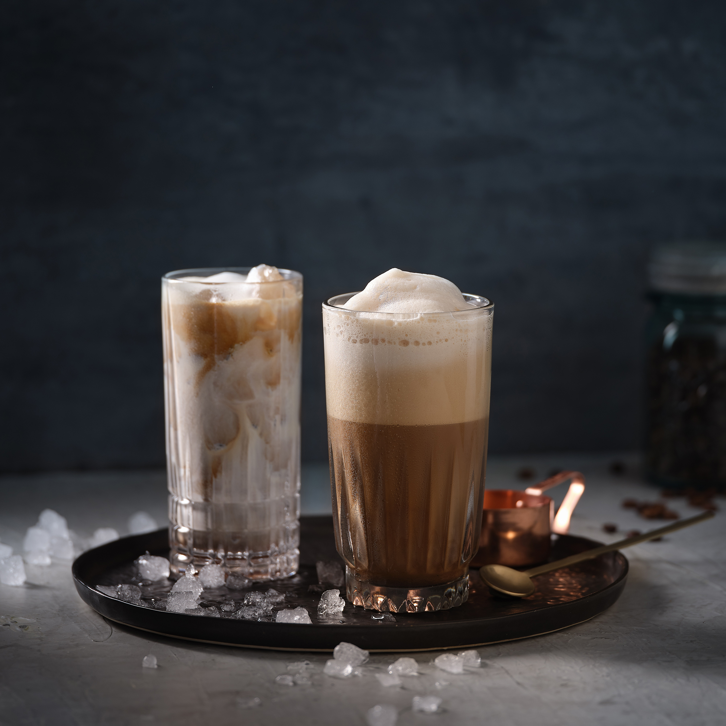 Iced Cafe und Eiskaffee sthen auf einem Tablett in dunklem Umfeld. Am Boden liegt Crushed Ice.