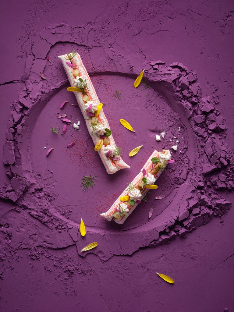 two meringue sticks with special pattern lie on purple powder. As decoration you can see petals