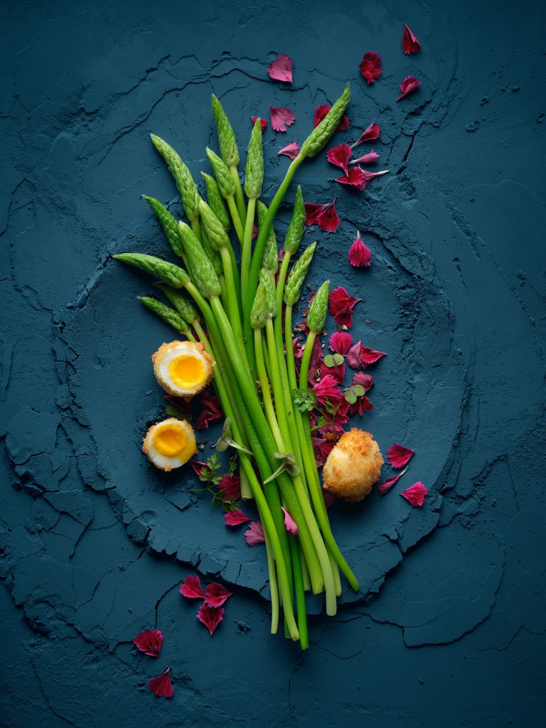 several green asparagus spears and open quail eggs lie on a dark blue powder background